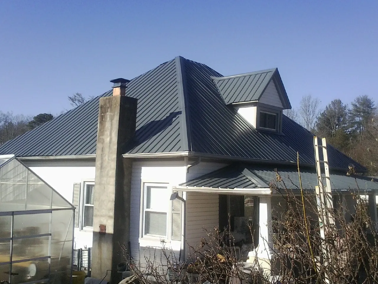 Dark blue standing seam metal roof on a white farmhouse with dormer — Slate & Tile Roof Repair by Roofing Brothers in Dunmor