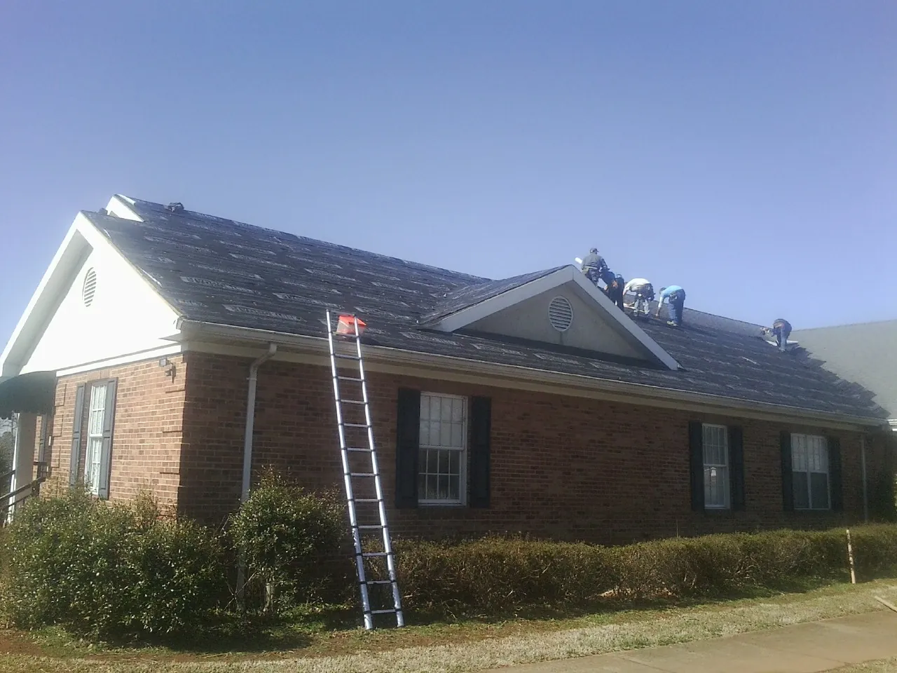 Crew tearing shingles off a brick ranch roof with a ladder set — Emergency Roof Repair work by our crew in Dunmor