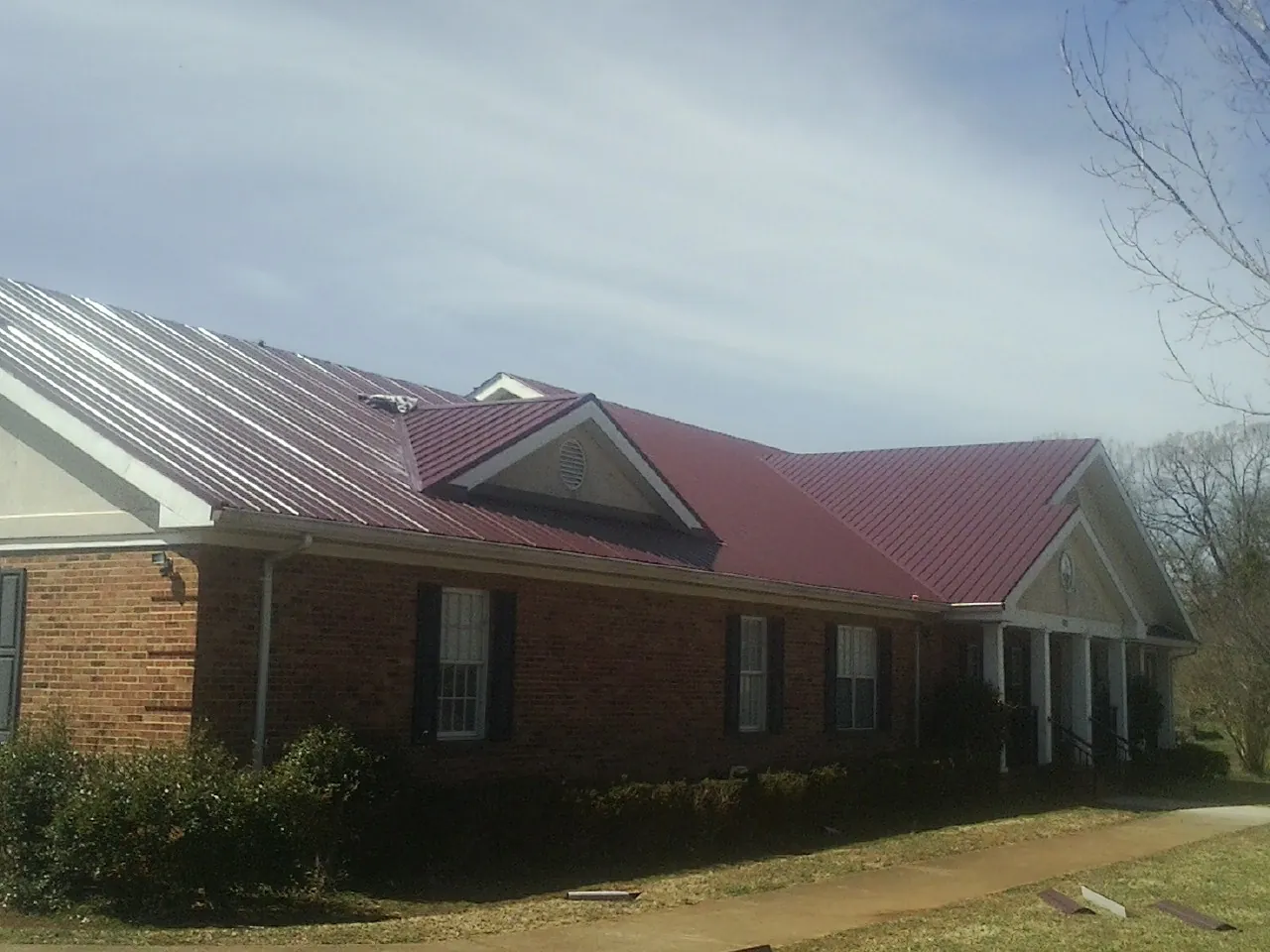 Red metal roof with gabled entries on a long brick building, from a Hail Damage Roof Repair job in Dunmor