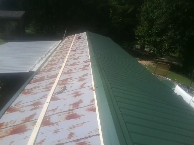 Old rusted panels beside newly installed green metal roofing — Wind Damage Roof Repair by Roofing Brothers in Dunmor