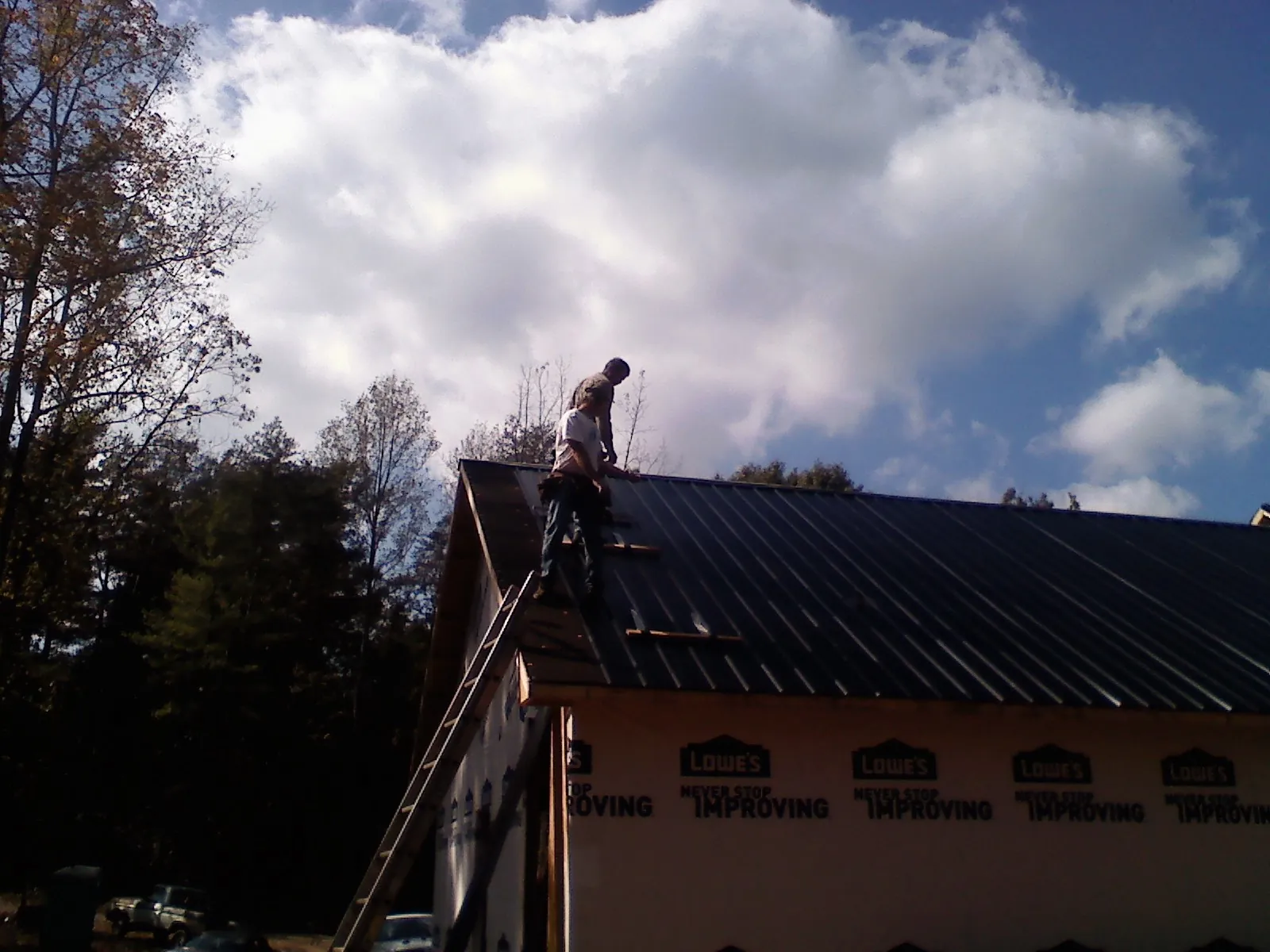Roofer fastening dark metal panels high against a cloudy sky, from a Roof Inspection job in Dunmor