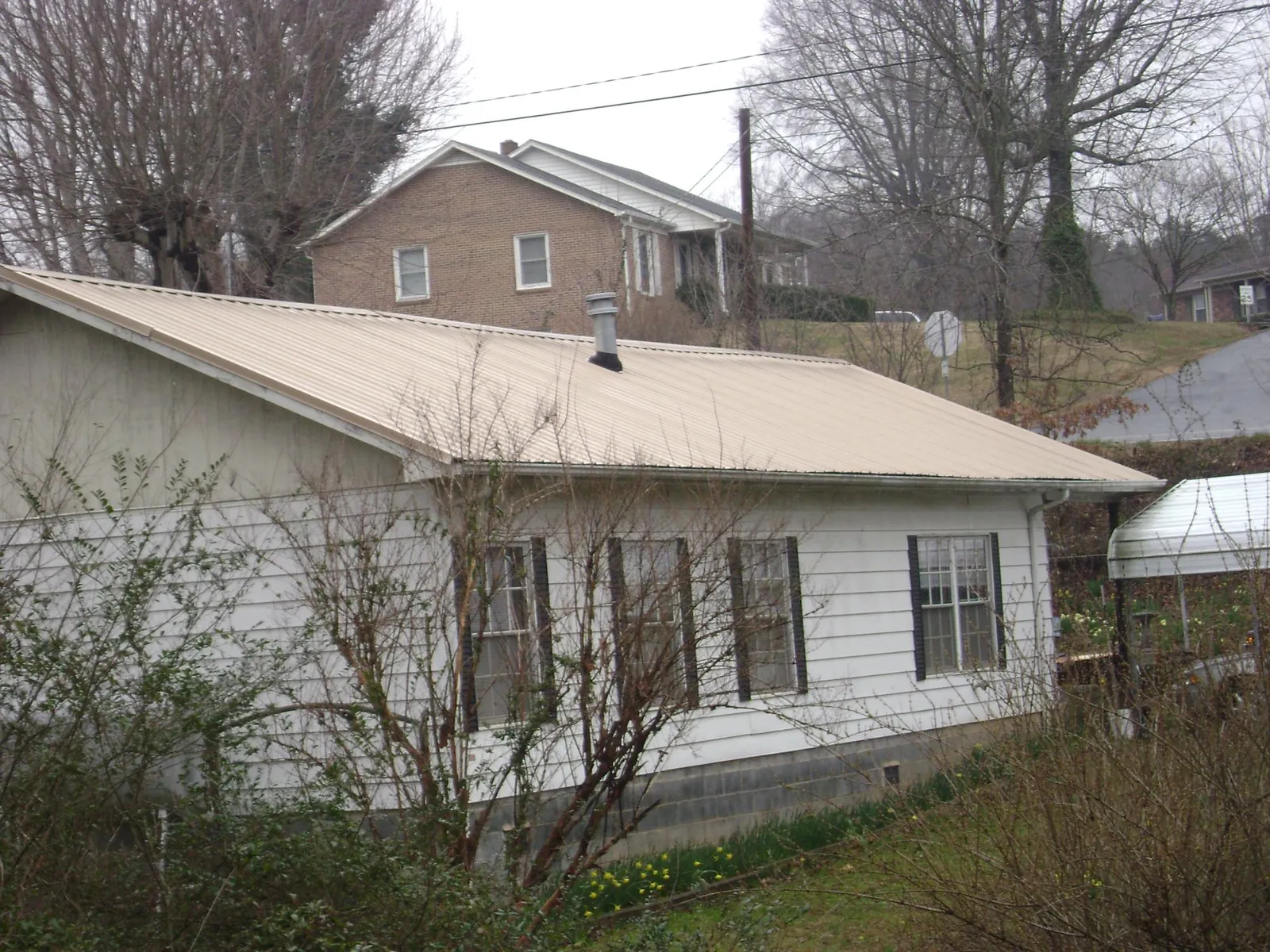 Tan metal roof on a white sided house set into a hillside — Commercial Roofing by Roofing Brothers in Dunmor